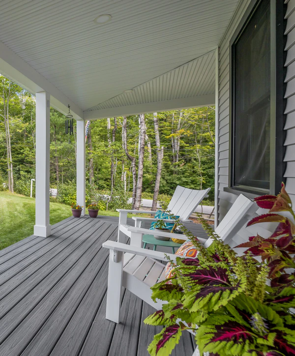 A relaxing covered porch featuring dark grey composite decking, white Adirondack chairs, and lush green landscaping, showcasing custom home additions in Cupertino, CA.