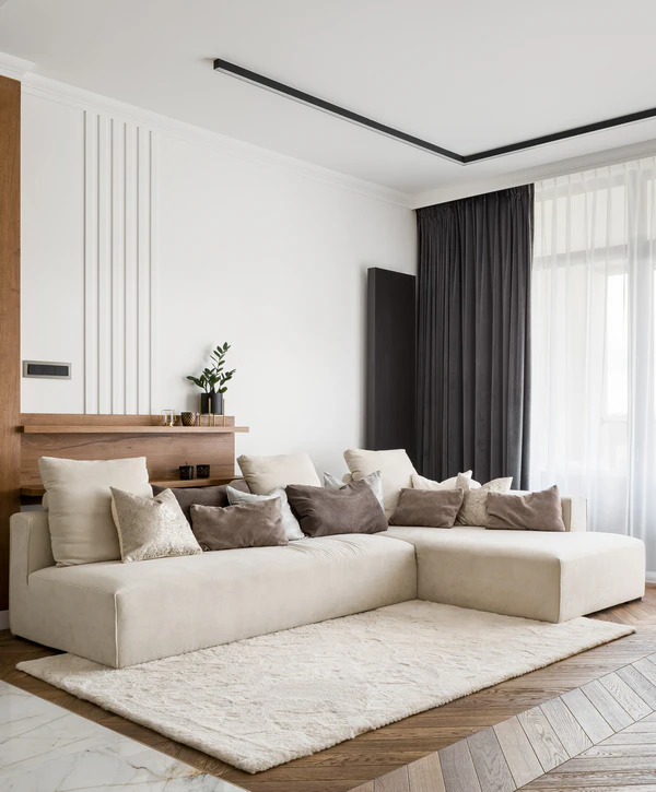 A minimalist modern living space featuring a large cream sectional sofa, textured rug, and architectural lighting, designed by top home addition companies in Cupertino, CA.